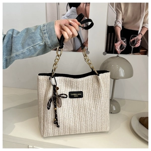 Detail of woven straw tote bag featuring V-shaped texture and gold metal chain strap