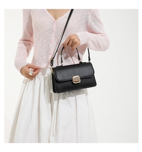 Detail of a black matte leather handbag with gold metal clasp and adjustable strap