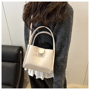 Detailed close-up of cream leather bucket bag with dual handles and unique buckle closure