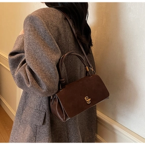 Side view of dark brown suede crossbody bag with gold twist lock on grey wool coat