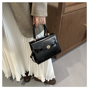Detail of elegant black glossy leather handbag with gold twist lock and adjustable strap