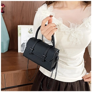 Détail d'un sac à main élégant en cuir noir avec chaîne métallique tenu par le mannequin