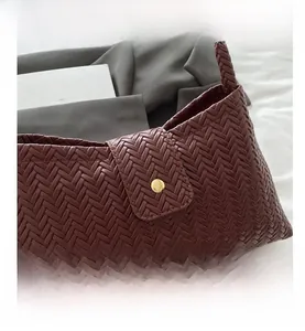 Detailed close-up of woven leather texture and gold snap closure on burgundy shoulder bag