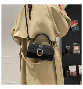 Detail of black sequined flap handbag with gold metal clasp on a beige trench coat