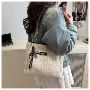 Close-up of beige straw tote bag featuring herringbone weave and black leather logo patch