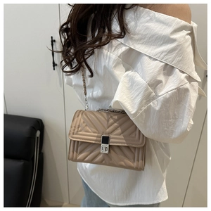 Detail showing the quilted beige crossbody bag with silver lock worn by model