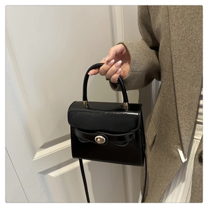 Detail view of black glossy mini square bag with golden twist lock on stylish coat