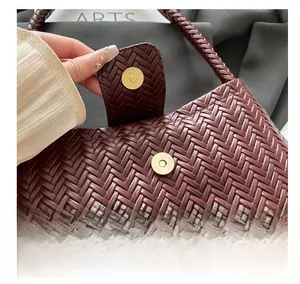 Close-up of woven wine red handbag featuring a glossy golden magnetic metal buckle closure