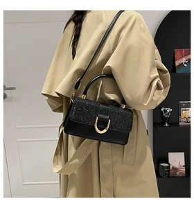 Detail of elegant black glitter handbag with golden U-shaped clasp worn over a beige coat