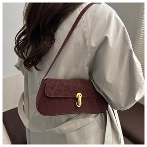 Détail du sac bandoulière bordeaux avec gaufrage léopard et fermoir doré sur un mannequin