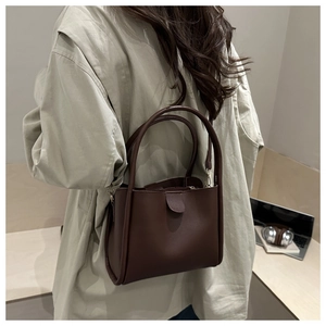Detail of a dark brown leather bucket bag worn crossbody in a minimalist office setting