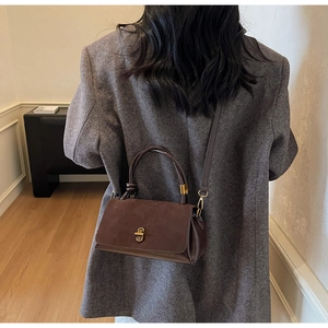 Brown suede crossbody bag detail showing matte texture and golden U-shaped buckle lock
