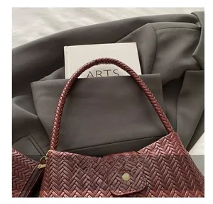 Close-up of burgundy woven leather shoulder bag with textured handle and flap detail