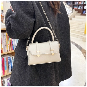 Détail du sac carré beige minimaliste avec boucle dorée et bandoulière chaîne porté
