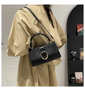 Detail of black crossbody bag featuring a glitter texture flap and gold U-shaped metal buckle