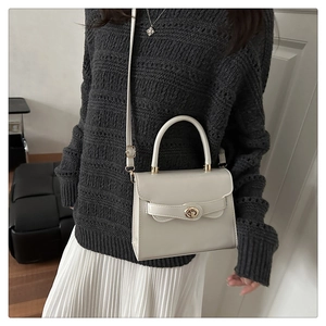 Detail of cream white crossbody box bag with gold swivel lock on grey knit sweater
