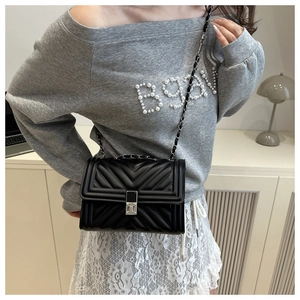 Detail of black quilted leather crossbody bag with silver chain strap on model