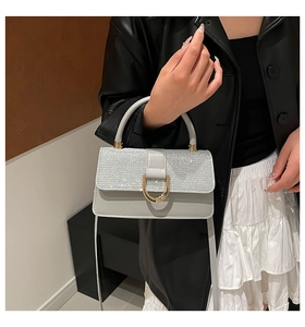 Close-up of sparkling silver rhinestones and gold buckle on a grey luxury square handbag