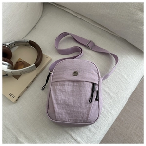 Minimalist purple nylon crossbody bag on a white sofa with fashion accessories