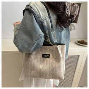 Detail of woven straw tote bag with black leather shoulder strap and gold chain accent