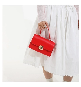 Close-up of a bright red handbag with elegant gold metal clasp on white dress