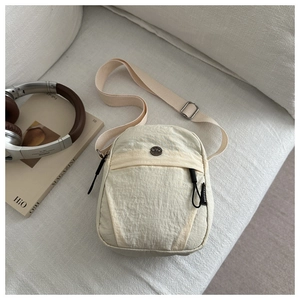 Detail of off-white nylon crossbody bag featuring pleated texture and round metal logo