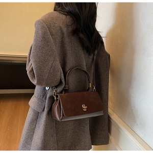 Brown suede crossbody bag worn over a grey tweed jacket in a warm autumn setting