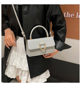 Close-up of gray handbag with silver glitter flap and gold D-ring buckle on leather jacket