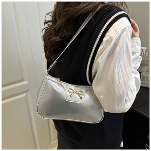 Silver metallic baguette bag with golden bow detail shown on a model's shoulder