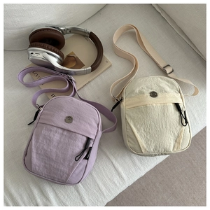 Close-up of minimalist nylon crossbody bags in purple and beige with metal logo