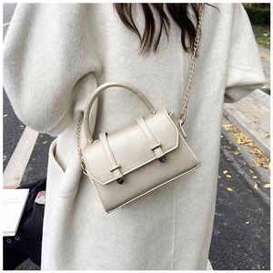 Sac bandoulière en cuir doré champagne avec chaîne porté sur un manteau clair en extérieur