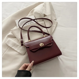 Detailed view of dark red leather square handbag with golden twist lock and bow detail