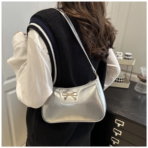 Close-up of a silver metallic baguette bag with a golden bow buckle on model shoulder