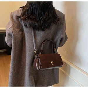 Detail view of brown suede patchwork handbag with a gold twist lock and a knotted handle