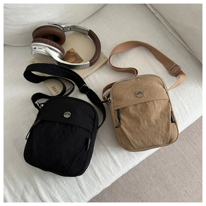 Detail of minimalist nylon crossbody bags in black and khaki on a white sofa