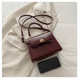 Detail of burgundy PU leather crossbody bag with decorative bow and golden twist lock