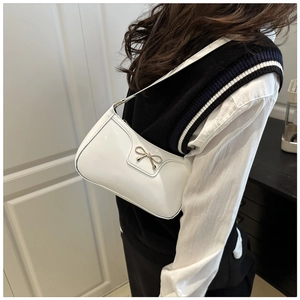 Detail of white patent leather underarm bag featuring a metallic gold bow buckle decoration