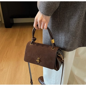 Detail of suede flap and leather body contrast on dark brown crossbody bag with gold lock