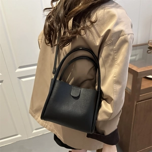 Minimalist black matte leather bucket bag shown as a crossbody on a stylish model