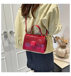 Detail of red crossbody bag with crocodile embossed flap and square buckle on model