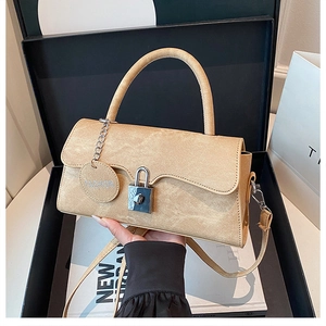 Details einer beige Crossbody-Tasche aus Leder mit silbernem Schloss und Anhänger