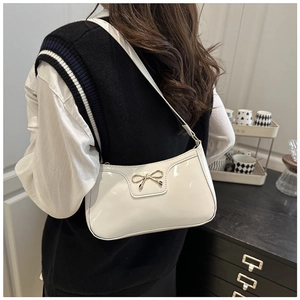 Close-up of white glossy PU underarm bag with gold bow knot and slim shoulder strap