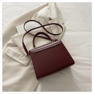 Detail of burgundy PU leather trapezoid handbag with gold metal clasp on a beige suit
