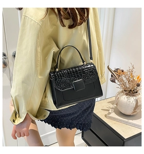 Detail of black crossbody bag with crocodile pattern flap and metal buckle on model