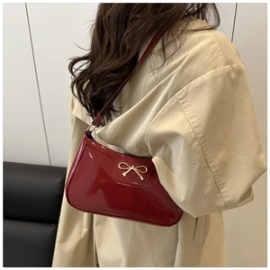 Detail of red patent leather shoulder bag with elegant gold bow metal ornament