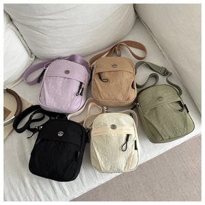 Detail view of colorful nylon crossbody bags with adjustable straps on a soft sofa