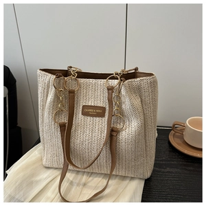 Detail of woven straw tote bag with brown leather handles and golden metal chain