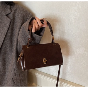 Detail of dark brown suede handbag with golden buckle and elegant knotted handle design