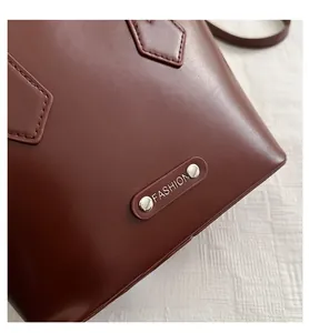 Close-up of brown textured leather bucket bag with oval metal FASHION emblem detail