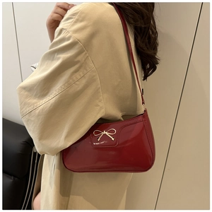 Close-up of red patent leather shoulder bag with a gold metal bow on a beige coat